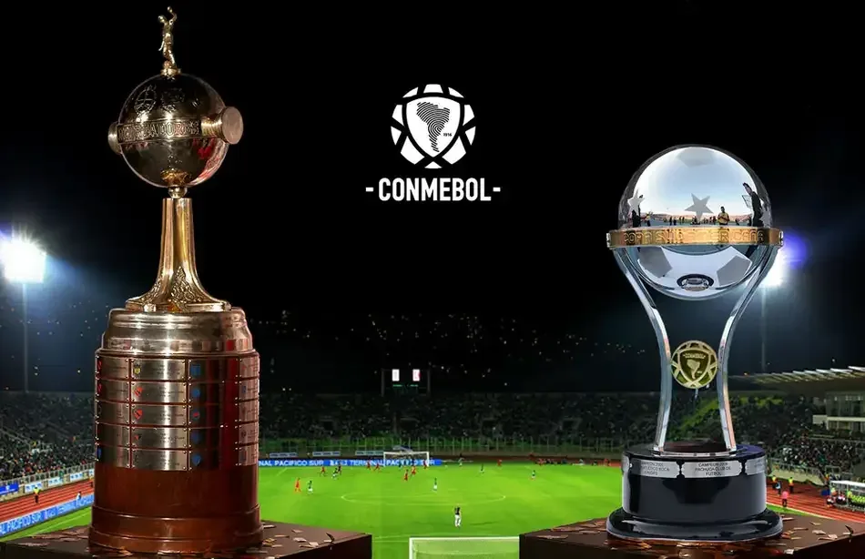 Os troféus da Copa Libertadores e da Copa Sul-Americana lado a lado com a logo da CONMEBOL ao centro, sobrepostos à foto de um estádio de futebol lotado à noite.