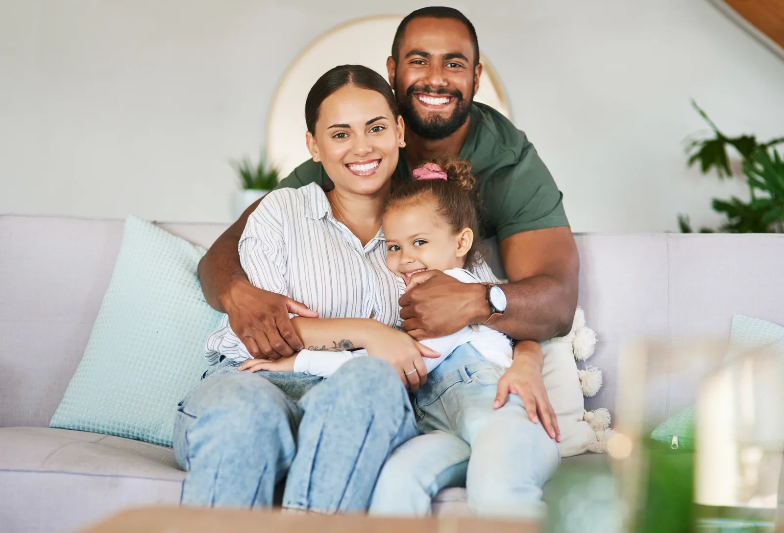 Dois adultos e uma criança abraçados no sofá de casa.