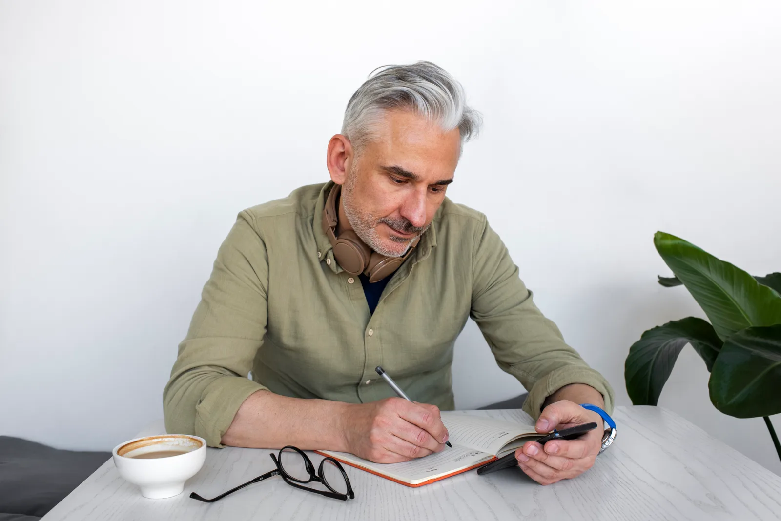 Homem com celular fazendo anotações em um caderno.