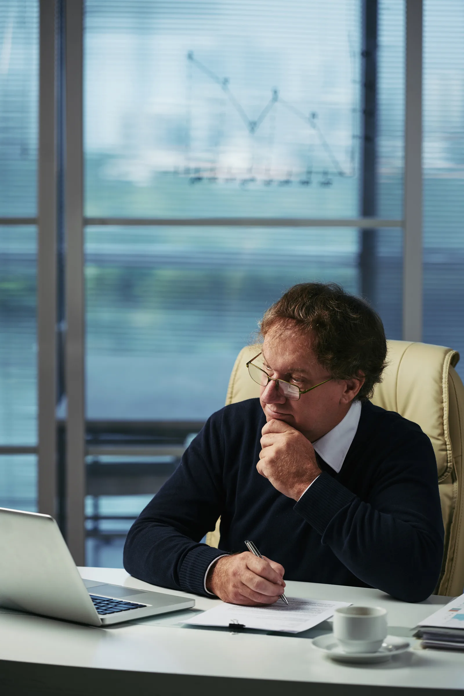 Homem conferindo documentos com um notebook sobre a mesa.